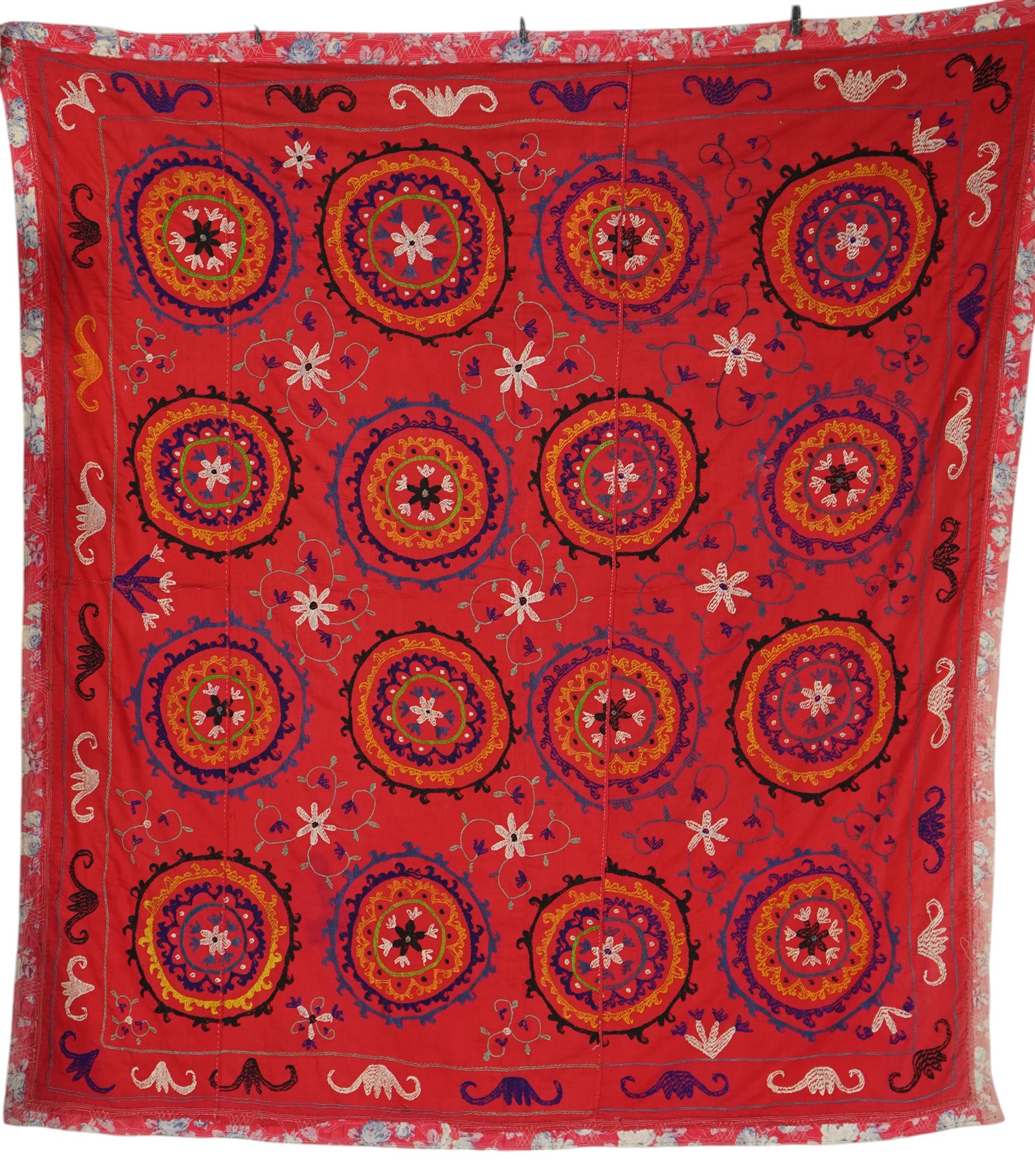 A large 20th century Uzbek multi coloured and embroidered Suzani wall hanging. The word Suzani meaning needlepoint in Farsi. Made in three panels embroidered on a rich dark red background, using large stylised multi colo